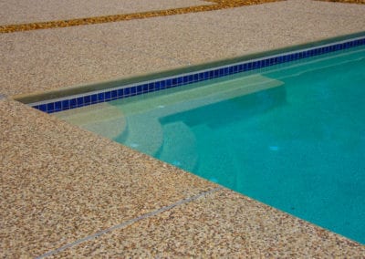 An outdoor swimming pool crafted by a reputable pool company with clear blue water and a surrounding pebbled deck.