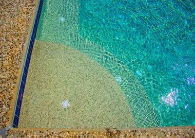 Swimming pool corner with clear blue water and textured underwater floor, built by a professional pool company.