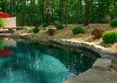 A serene backyard setting with a swimming pool designed by a top swimming pool company and landscaped garden, featuring a basketball hoop in the background.