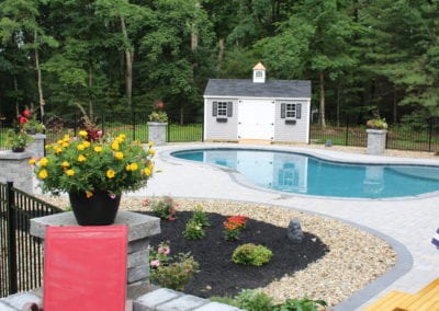 Backyard with a swimming pool installed by a top pool company and a small shed, surrounded by landscaped garden and trees.