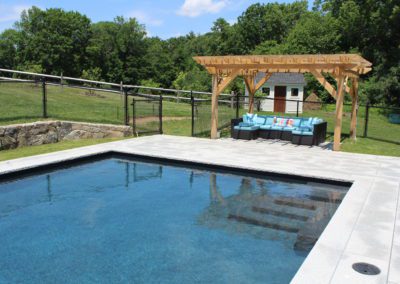 Swimming pool company-designed swimming pool with adjacent pergola and seating area in a landscaped backyard.
