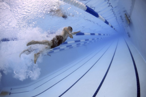 Two swimmers compete in a pool, captured underwater as they race side by side in separate lanes, their strokes creating bubbles and motion against the freshly replastered surface.