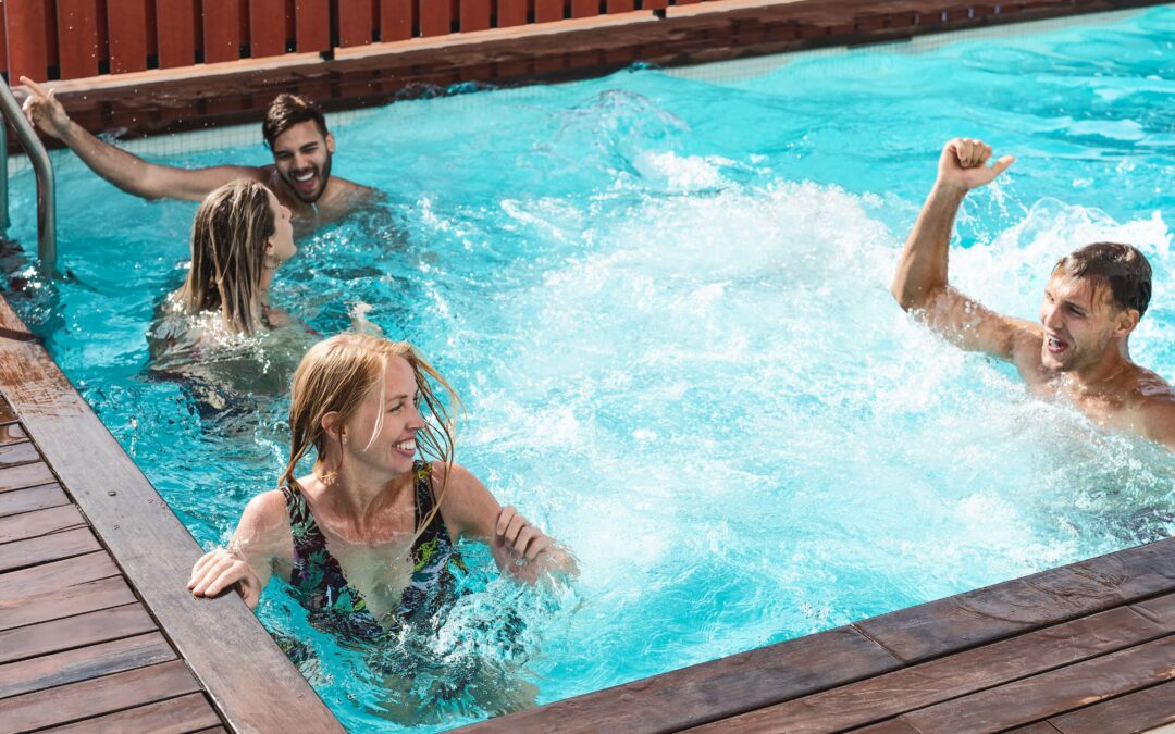 Four people enjoying themselves in an outdoor pool, with two of them standing in the water and two sitting at the edge.