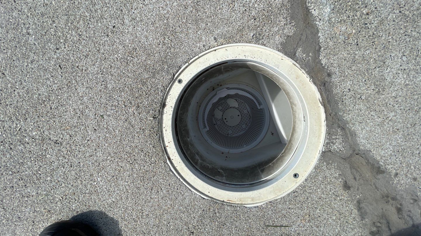 2 Close-up view of a circular pool drain embedded in textured concrete, with part of a foot barely visible at the bottom left edge of the image.