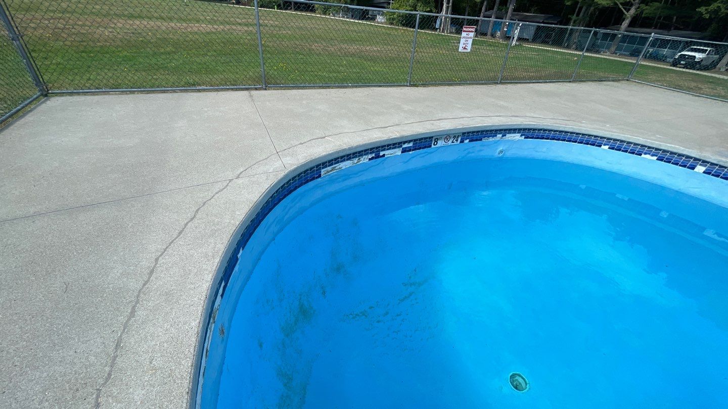 4 A partially empty swimming pool with visible cracks in the surrounding concrete and a chain-link fence enclosing the area.