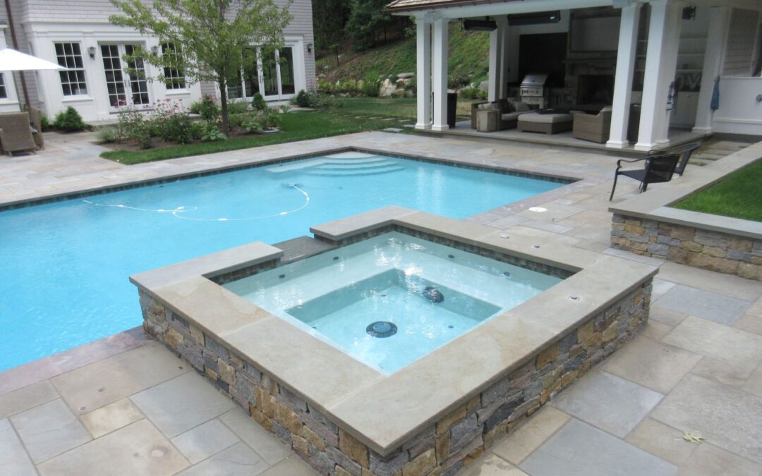Transform your backyard pool with a stone-bordered hot tub adjacent to a rectangular swimming pool, plus a patio area and a covered outdoor lounge.